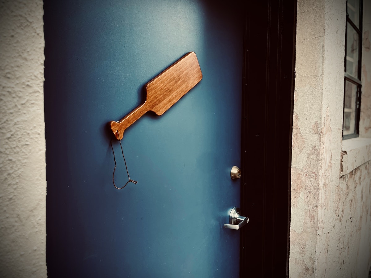 A wooden paddle hanging on a blue door