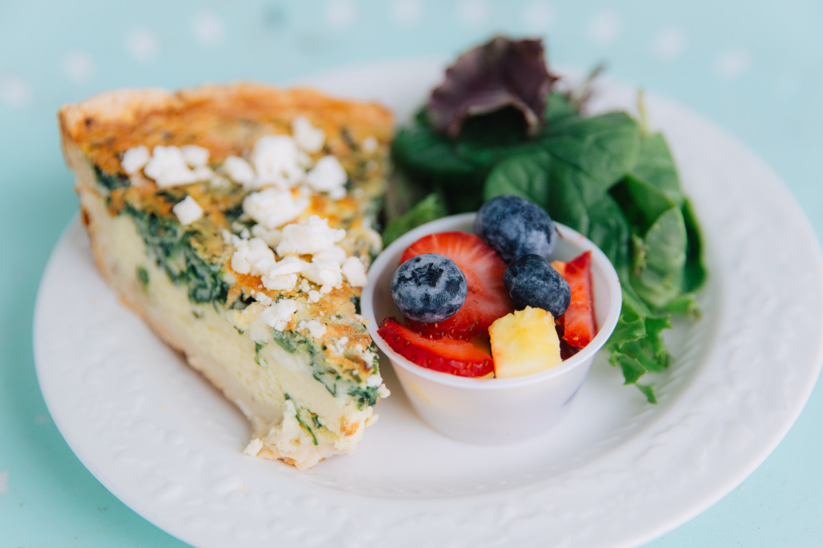 served a slice of quiche, accompanied by a bowl of assorted fresh fruit