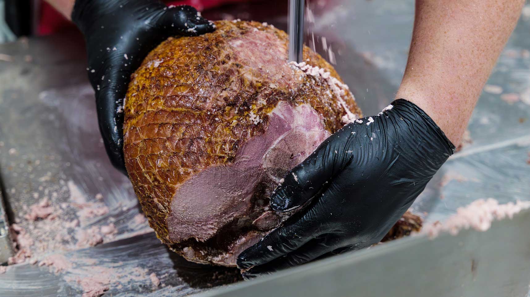 Person in black gloves slicing meat