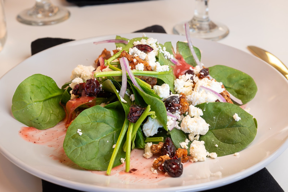 A plate of spinach salad with cranberries and feta cheese.