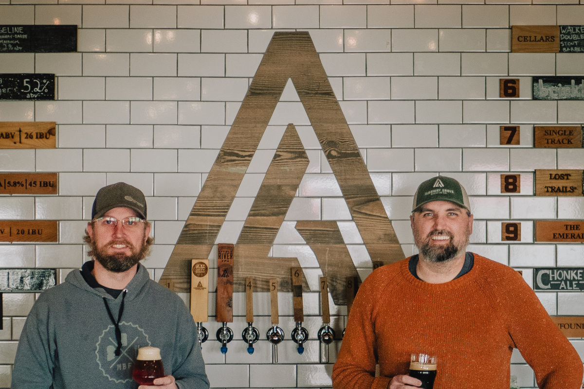 Two men smiling at a brewery bar, holding beer glasses