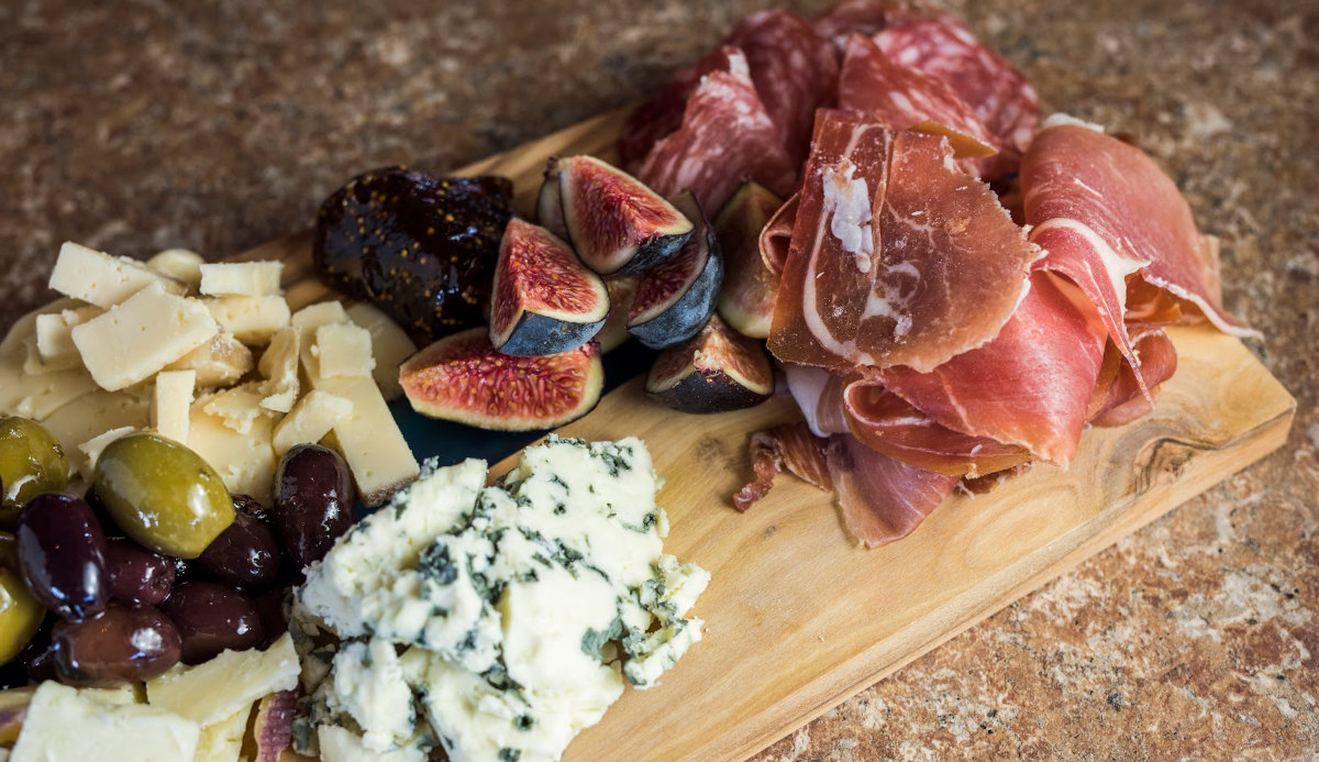 A wooden board displaying an assortment of meats and cheeses