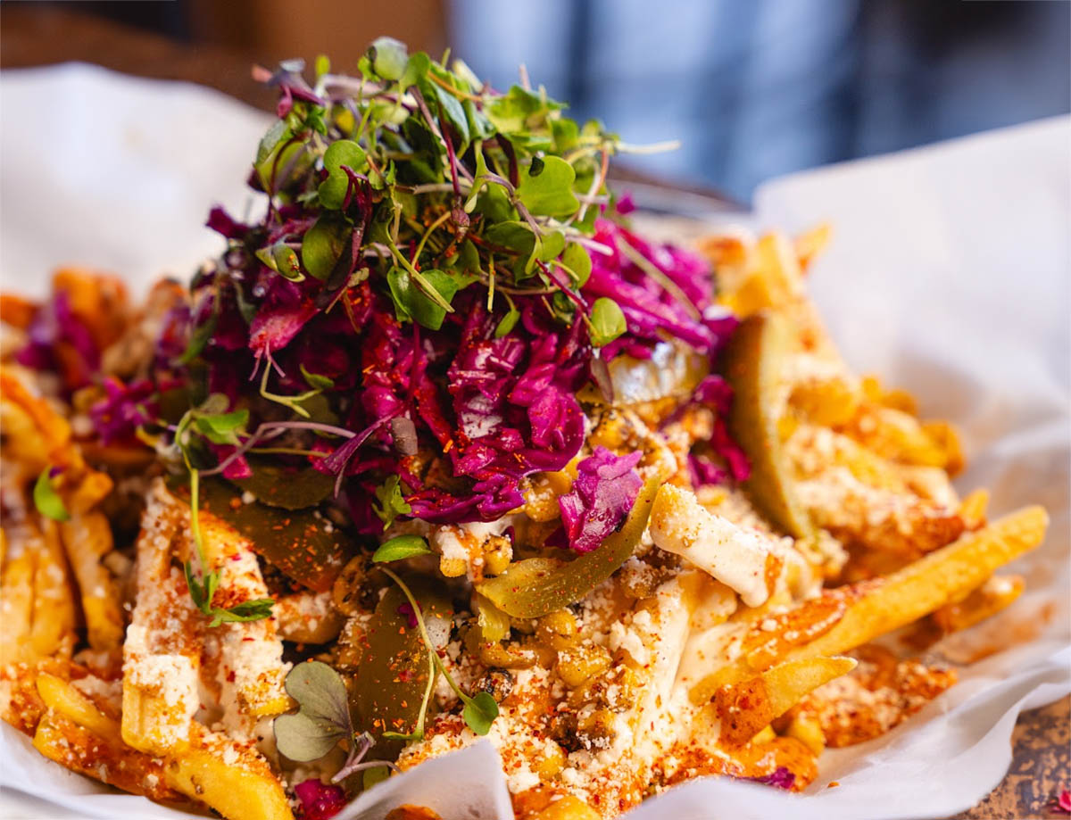 Loaded fries topped with cabbage, pickles, cheese, and microgreens on parchment paper