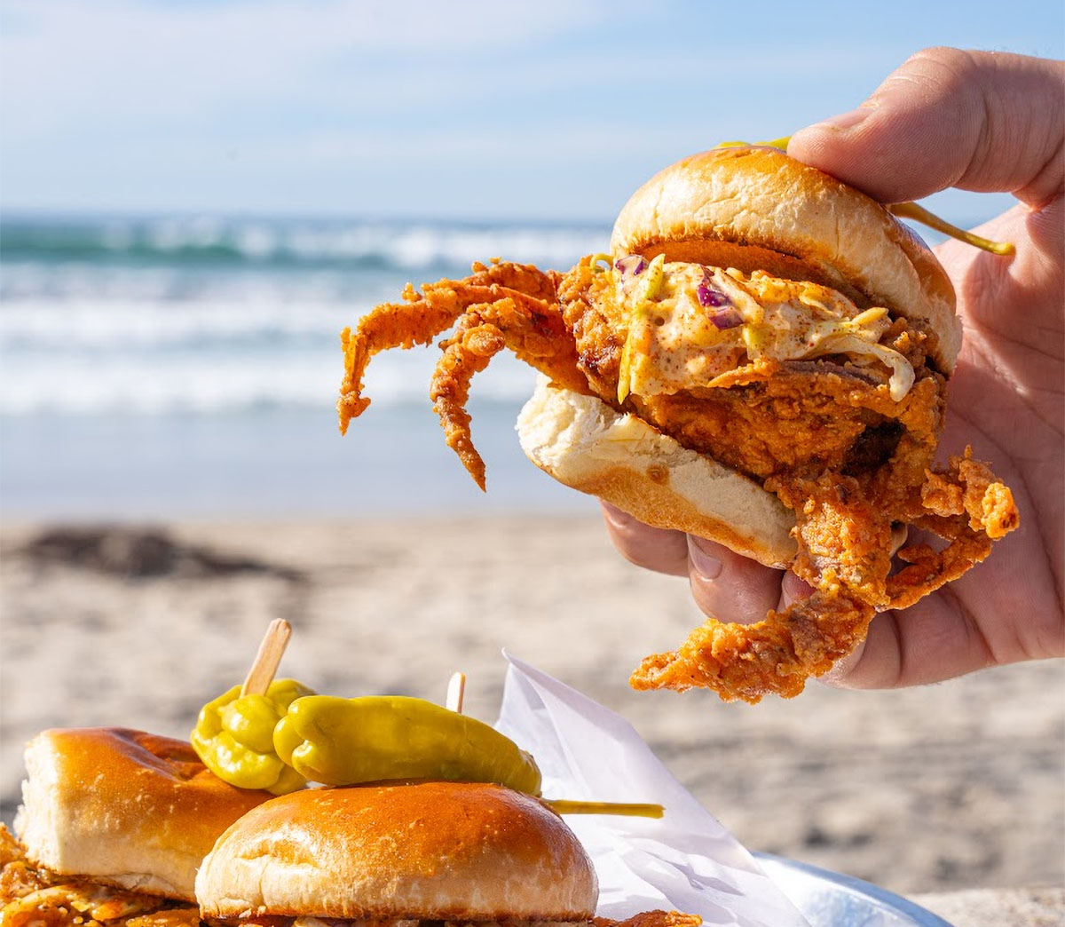 Hand holding a fried soft-shell crab sandwich on a beach