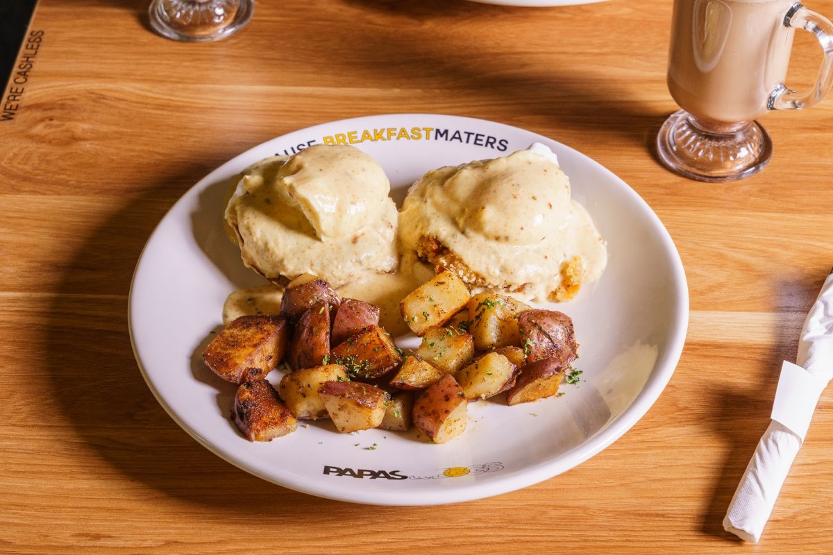 A white plate with biscuits topped with gravy and a serving of roasted potatoes.