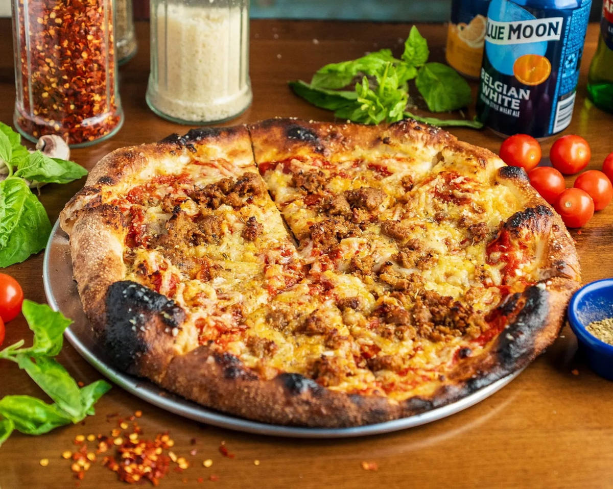 A delicious pizza topped with meat and cheese, placed on a wooden table, ready to be enjoyed.