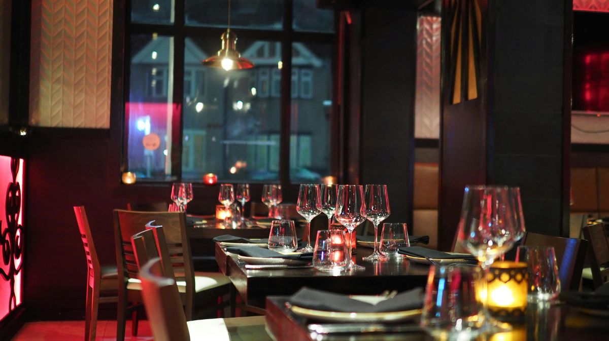 A cozy restaurant illuminated by red light, featuring a table set with elegant wine glasses.