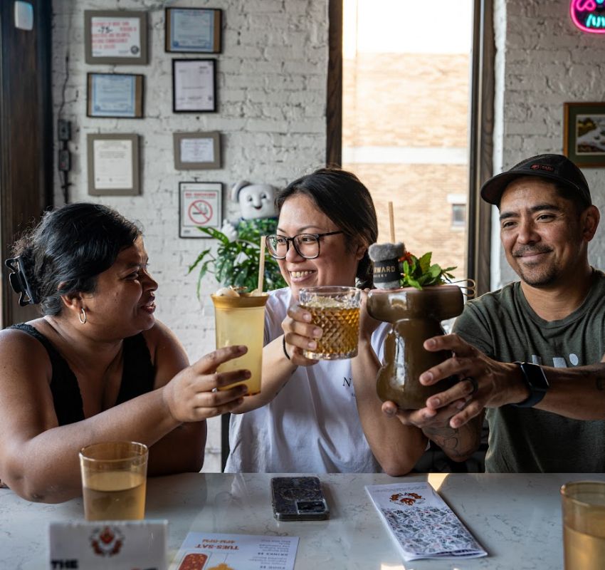 A group of three friends cheerfully toasting with diverse beverages in a cozy café setting.