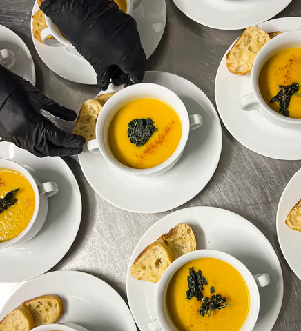 A person in black gloves holding a bowl of soup.