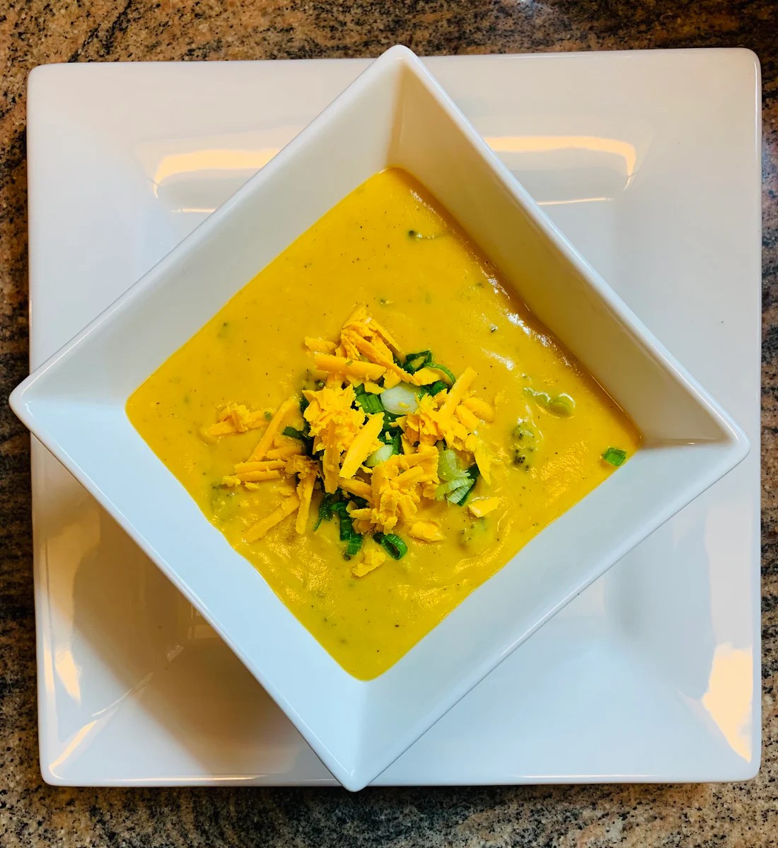 Creamy Broccoli Cheddar Soup topped with melted cheese and garnished with green onions.