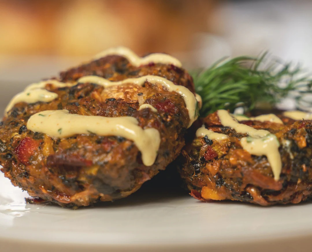 Two vegan sliders with meatball-shaped patties, topped with sauce, served on a white plate.