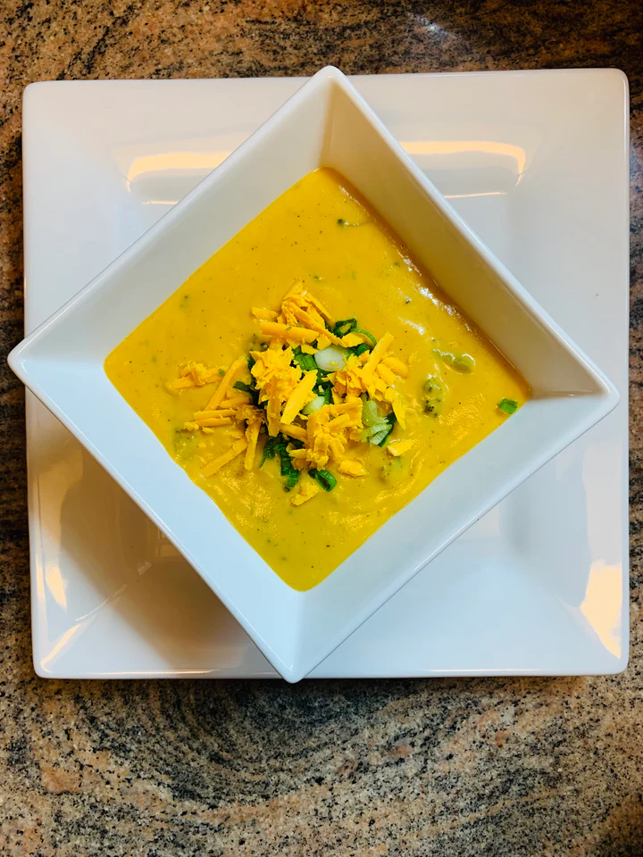 Creamy Broccoli Cheddar Soup topped with melted cheese and garnished with green onions.