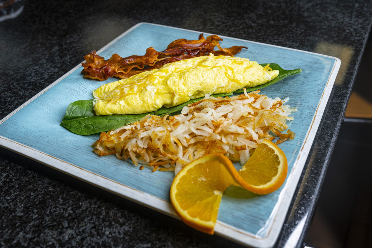 A breakfast plate displaying a fluffy omelet, savory bacon, and a fresh slice of orange