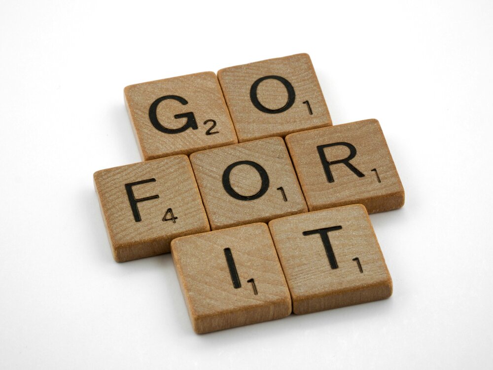 Scrabble tiles spelling out 'go for it' on a wooden board.