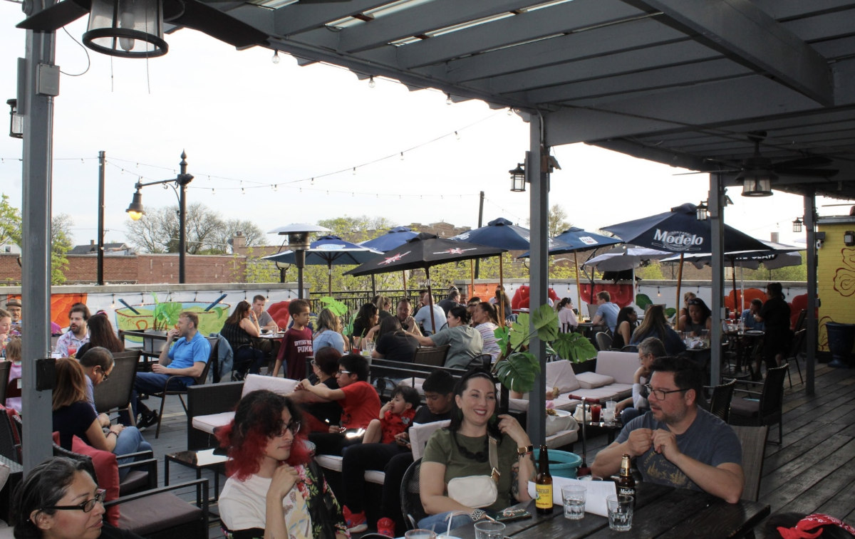 People dining al fresco, sitting at tables on a patio, surrounded by greenery