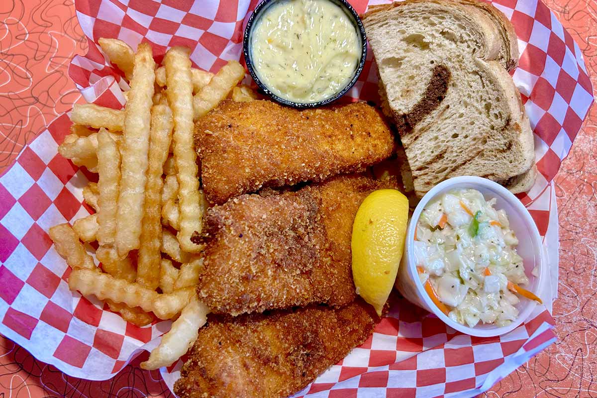 Fried fish and fries served with coleslaw, tartar sauce, and rye bread