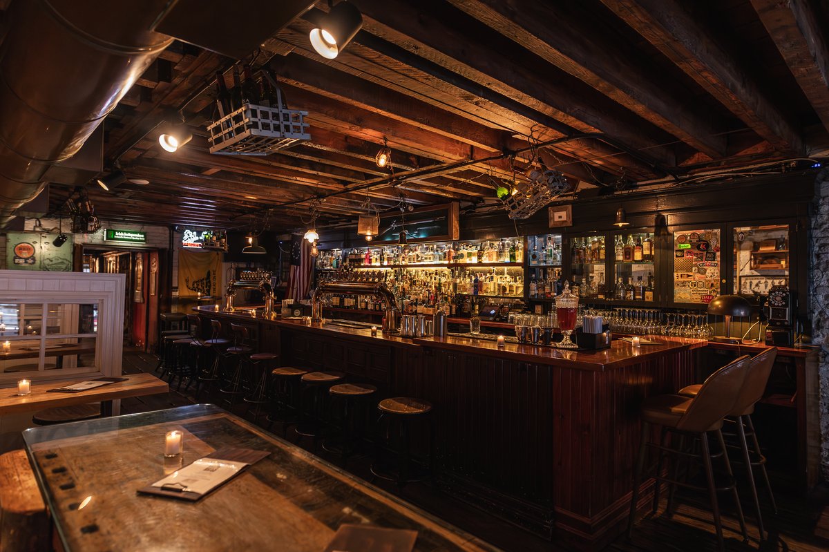 Dimly lit pub with a classic wooden bar and numerous liquor bottles on shelves.
