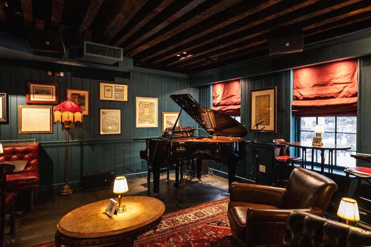 Cozy pub interior with a grand piano, framed pictures, leather seating, and warm lighting.