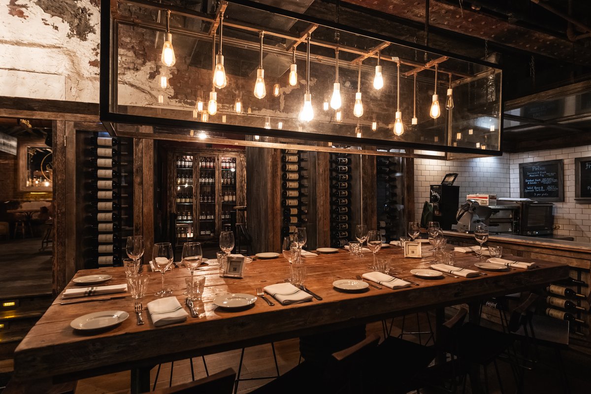 Long communal table set for dining, surrounded by wine racks and reflective decor.