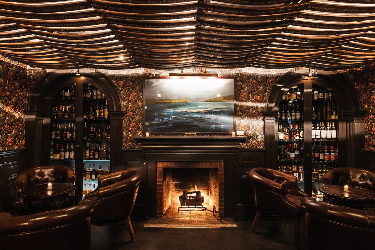 Bar interior with a large fireplace, leather armchairs, shelves with bottles.