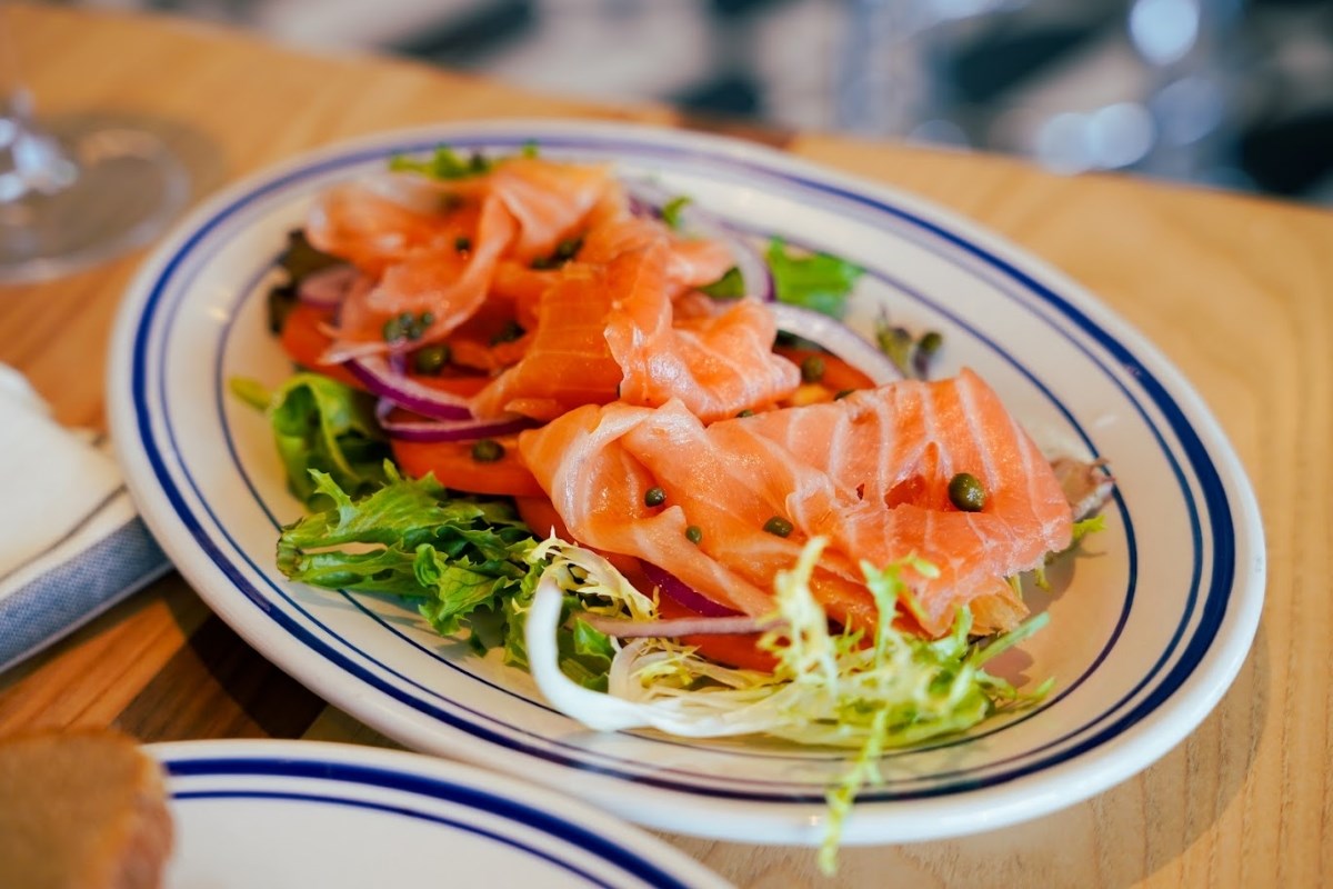 A plate of fresh, thinly sliced salmon served on a bed of mixed greens