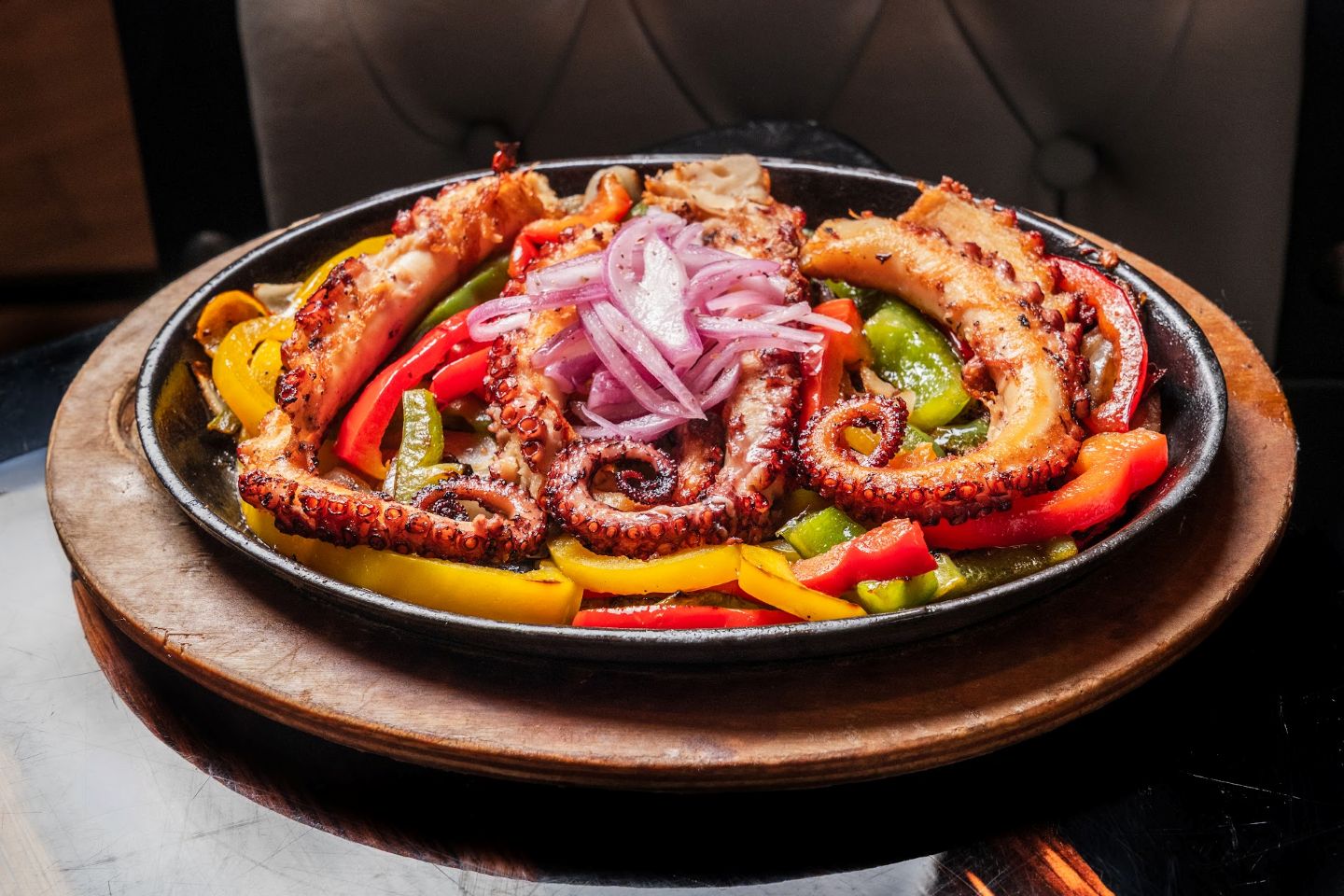 Grilled octopus with bell peppers and red onions in a cast-iron skillet.