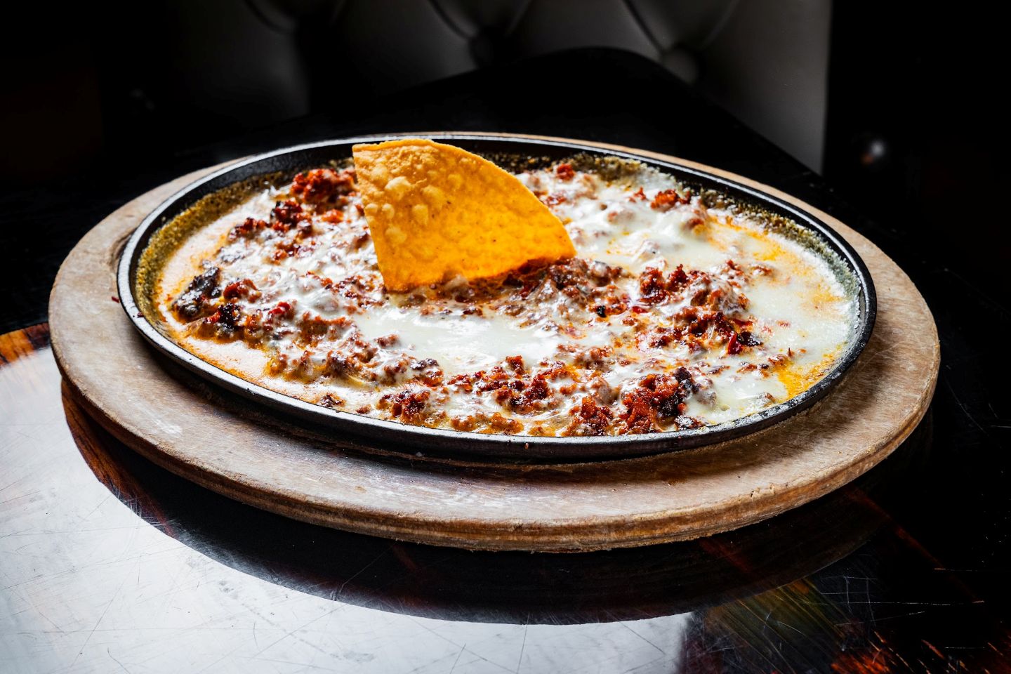 Creamy melted cheese dip topped with seasoned meat and a tortilla chip.