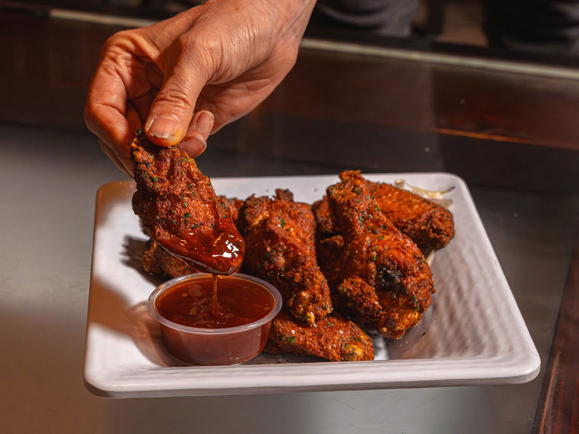 A hand holding a fried chicken wing dripping with barbecue sauce.