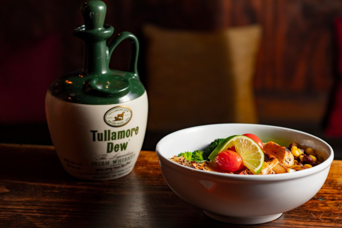 Whiskey bottle and bowl with food on a table.