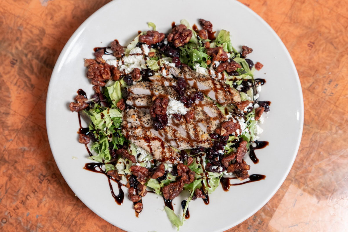 A salad with grilled chicken, mixed greens, and cheese crumbles on a white plate