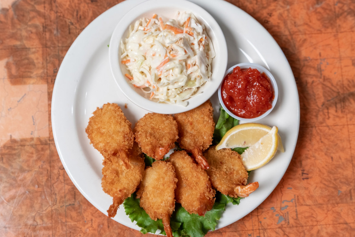 A plate with breaded fried shrimp, coleslaw in a bowl, cocktail sauce, and lemon wedges