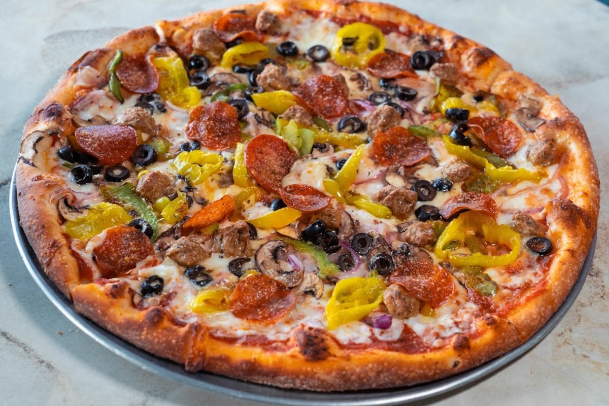 A pizza with pepperoni, peppers and olives on a plate.