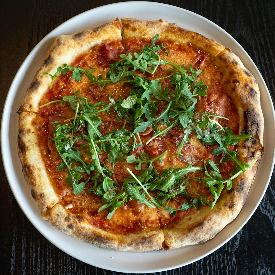 A pizza topped with prosciutto, melted cheese, and a generous amount of fresh arugula.