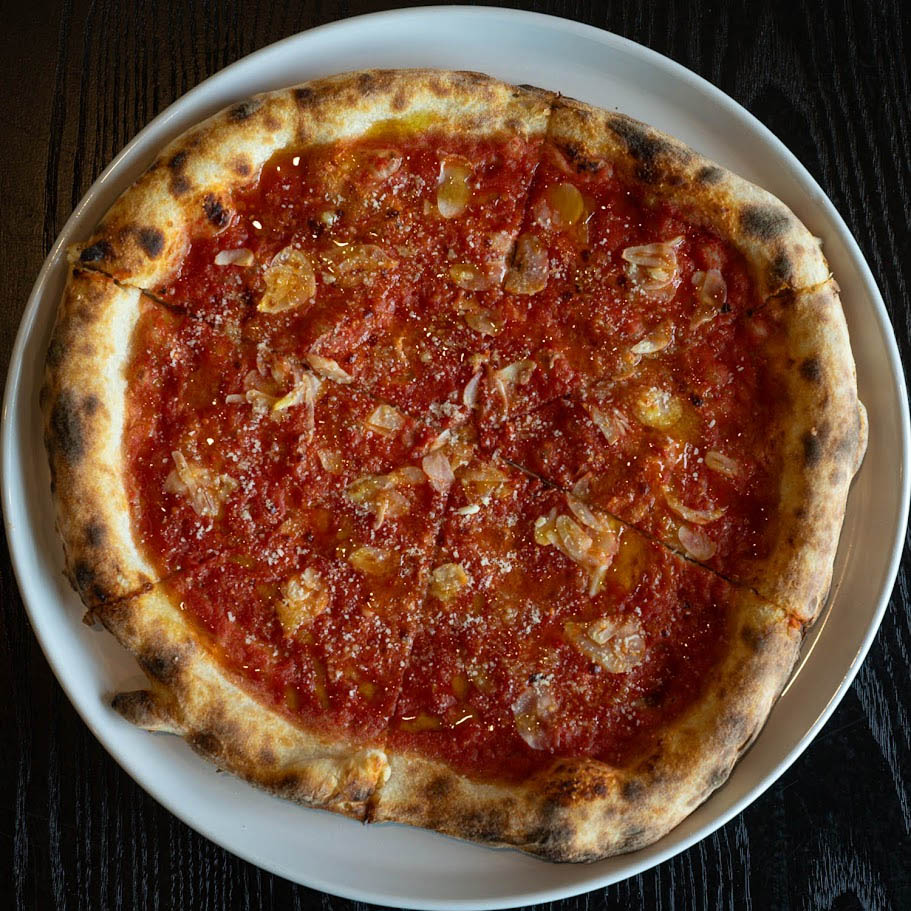 A close-up of a pizza with red sauce, sliced garlic, and a sprinkle of grated cheese.