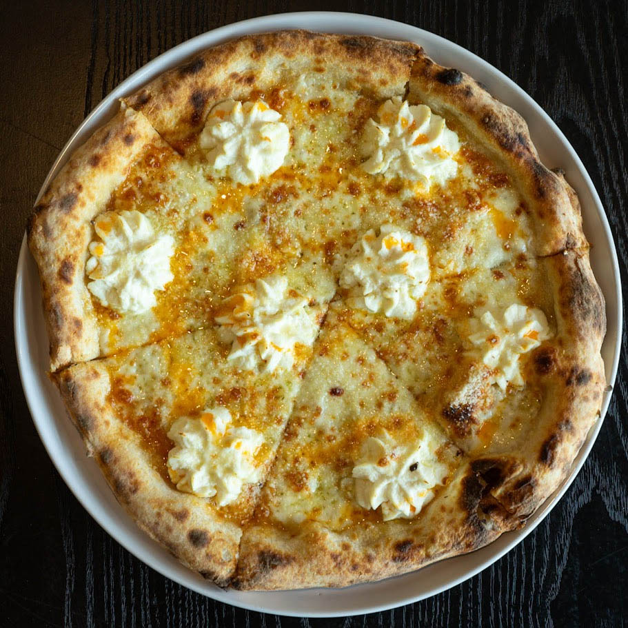 A sliced white pizza with dollops of creamy ricotta cheese and a drizzle of hot honey.