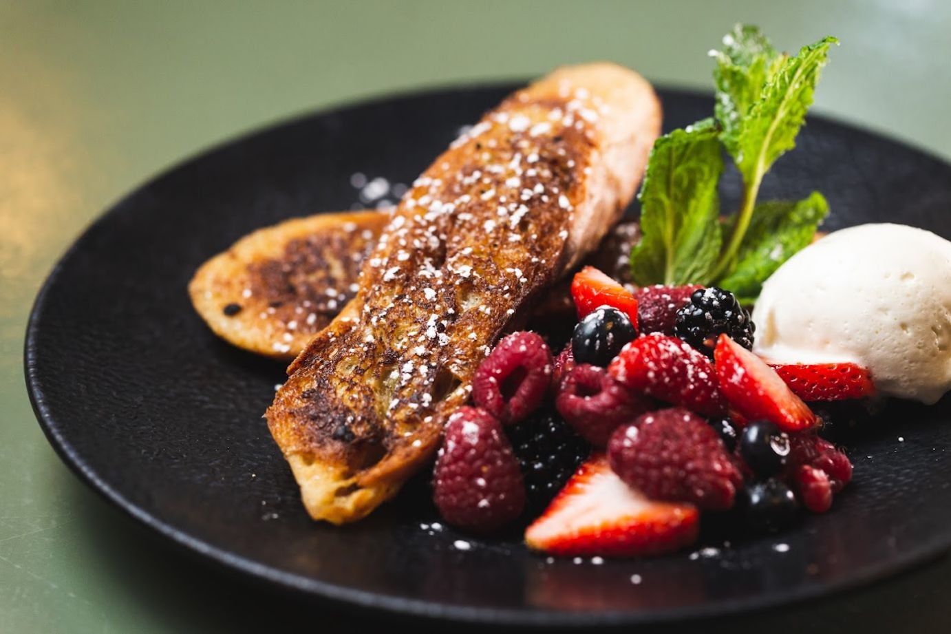 French toast with powdered sugar and fresh berries, butter and mint leaf garnish