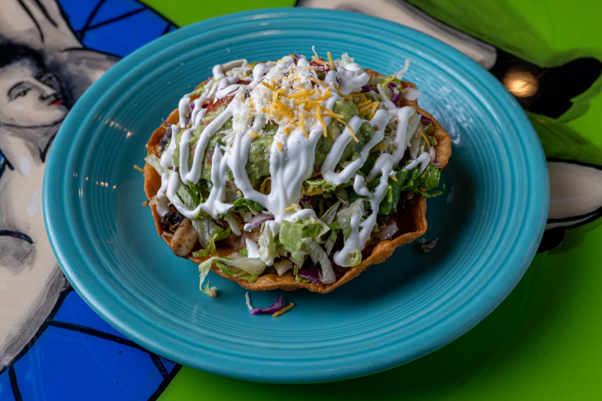 Crisp taco with lettuce, tomatoes, beans, cheese, sour cream, and guacamole on a blue plate