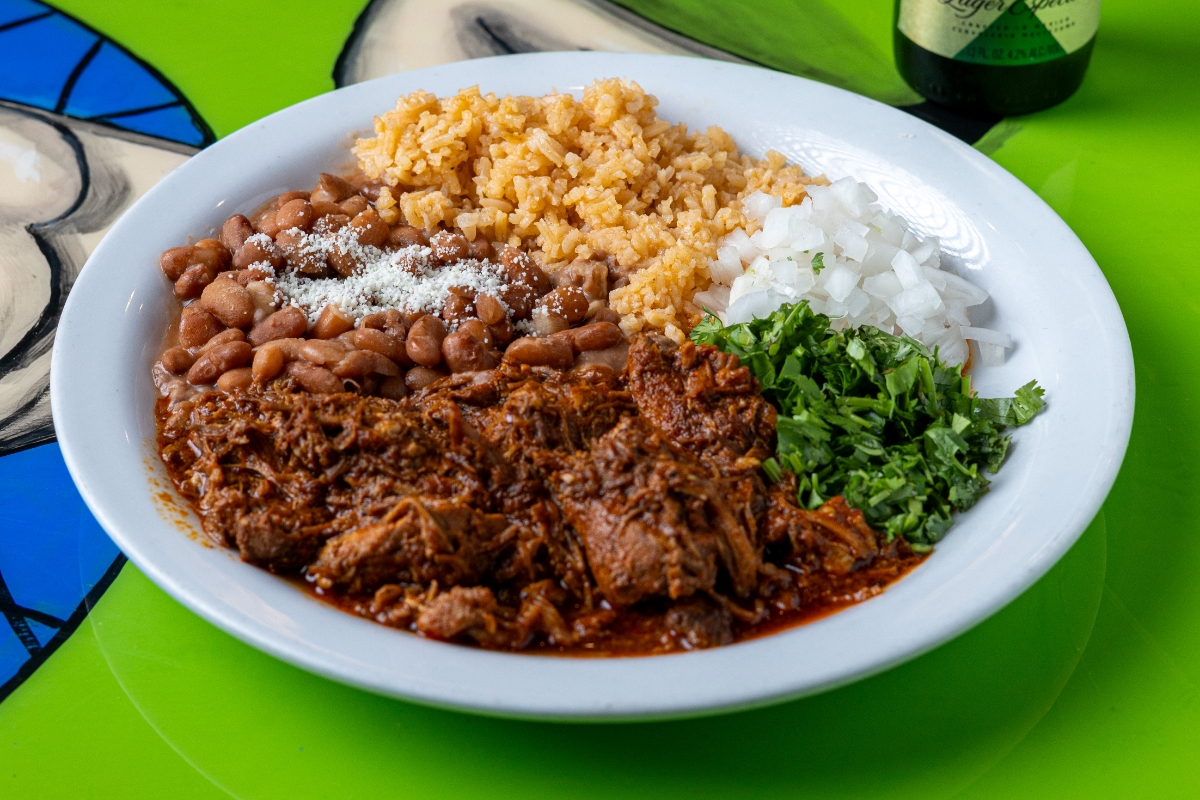 Plate with shredded beef in red sauce, pinto beans, rice, chopped onions, and cilantro