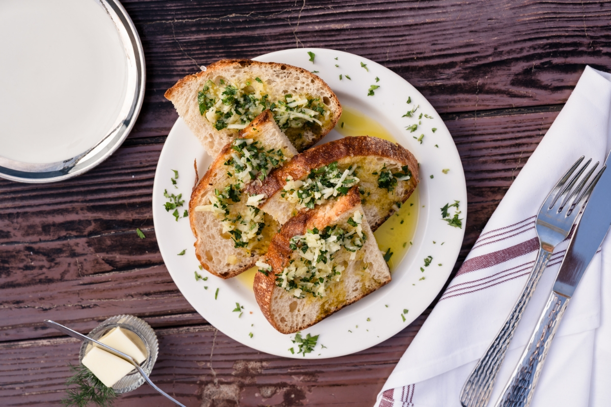 A plate of sliced bread topped with chopped herbs and garlic