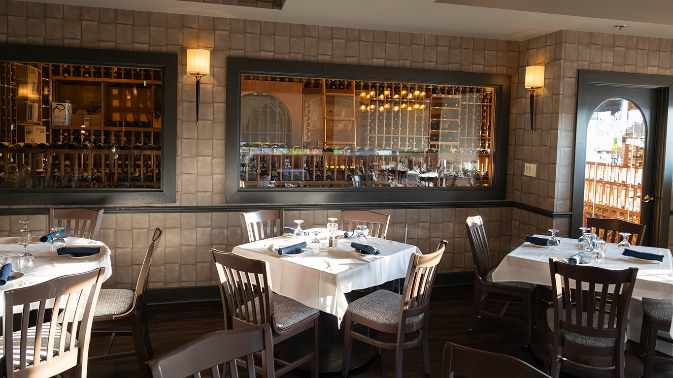 Restaurant tables set with white linens beside glass wine cellar wall