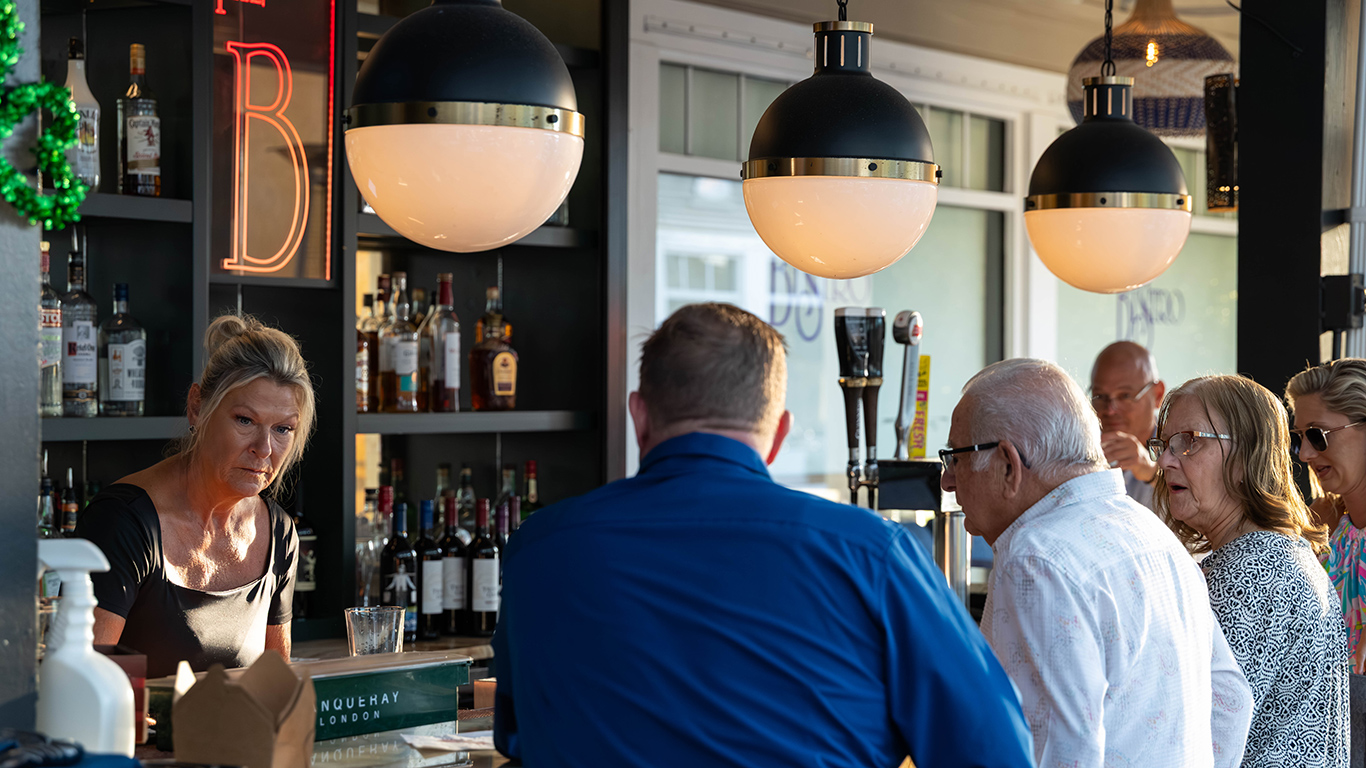 Bartender serving customers at modern bar with pendant lights