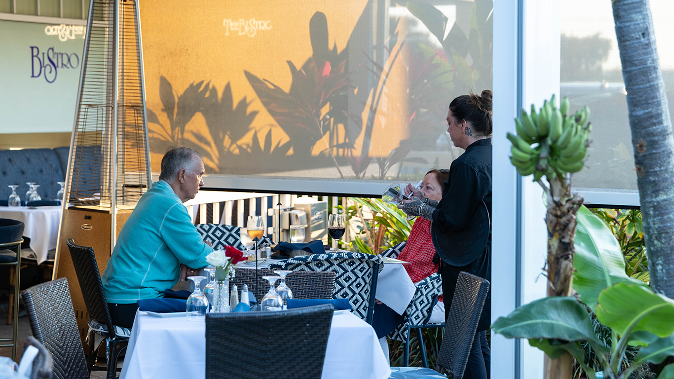 Server pouring wine for couple dining on outdoor patio at sunset