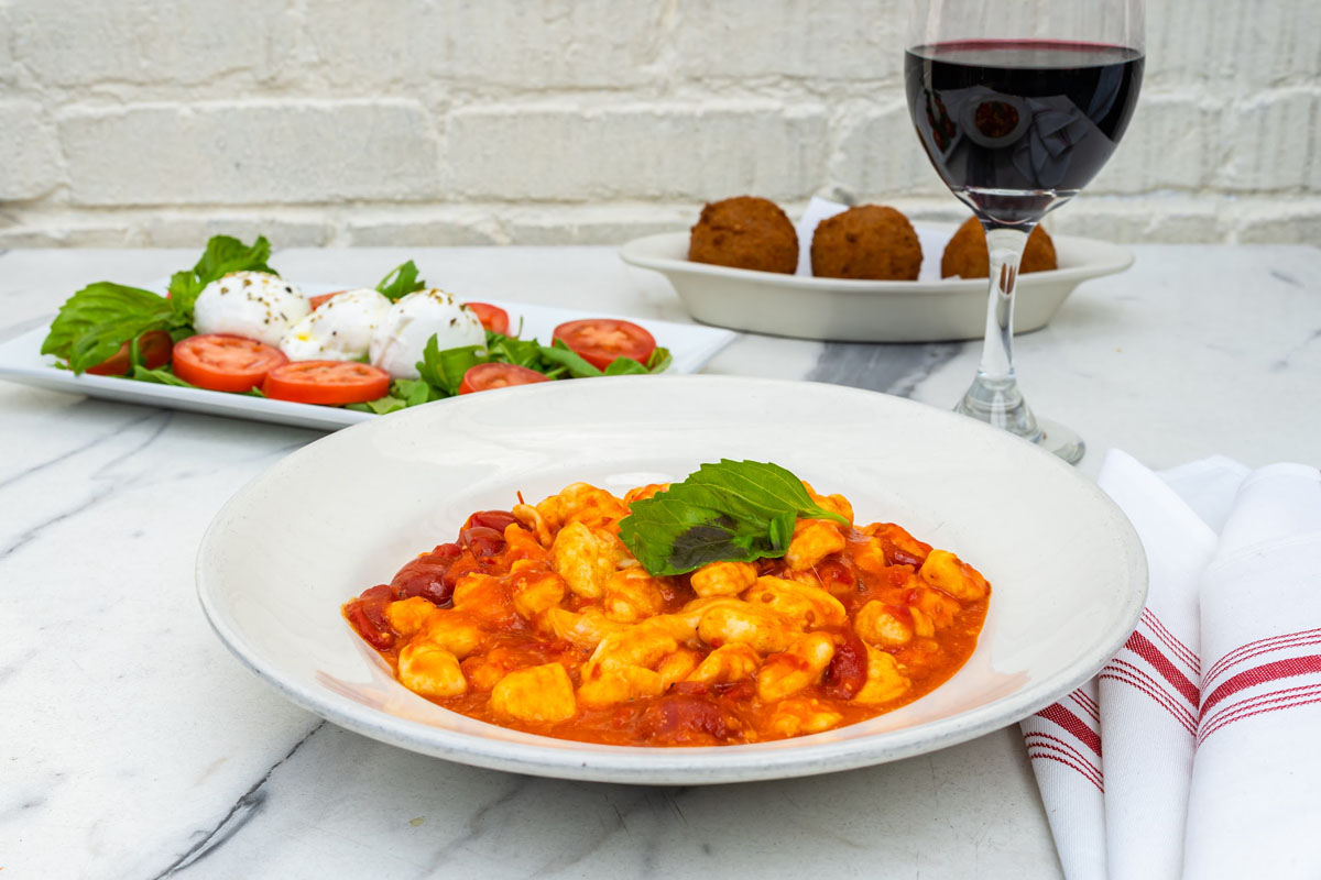 A plate of Gnocchi, Burrata salad, Arancini balls and red wine
