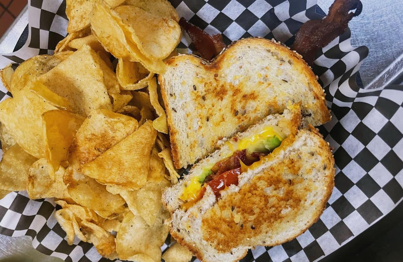 Closeup of a grilled cheese sandwich with chips and bacon on the side