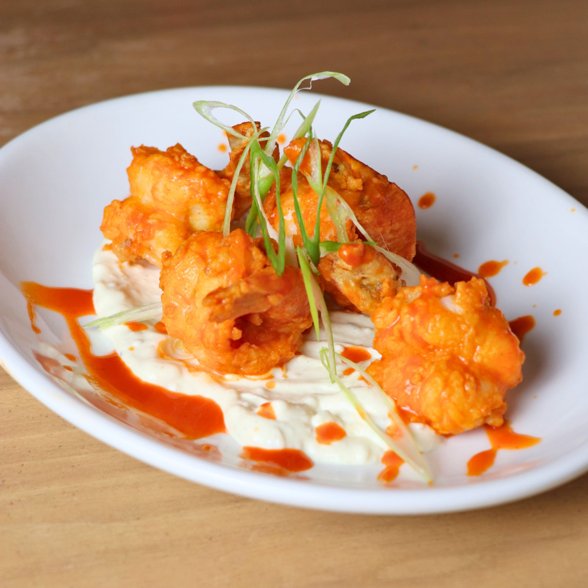 Buffalo fried shrimp on a white plate with a creamy sauce and green onion garnish