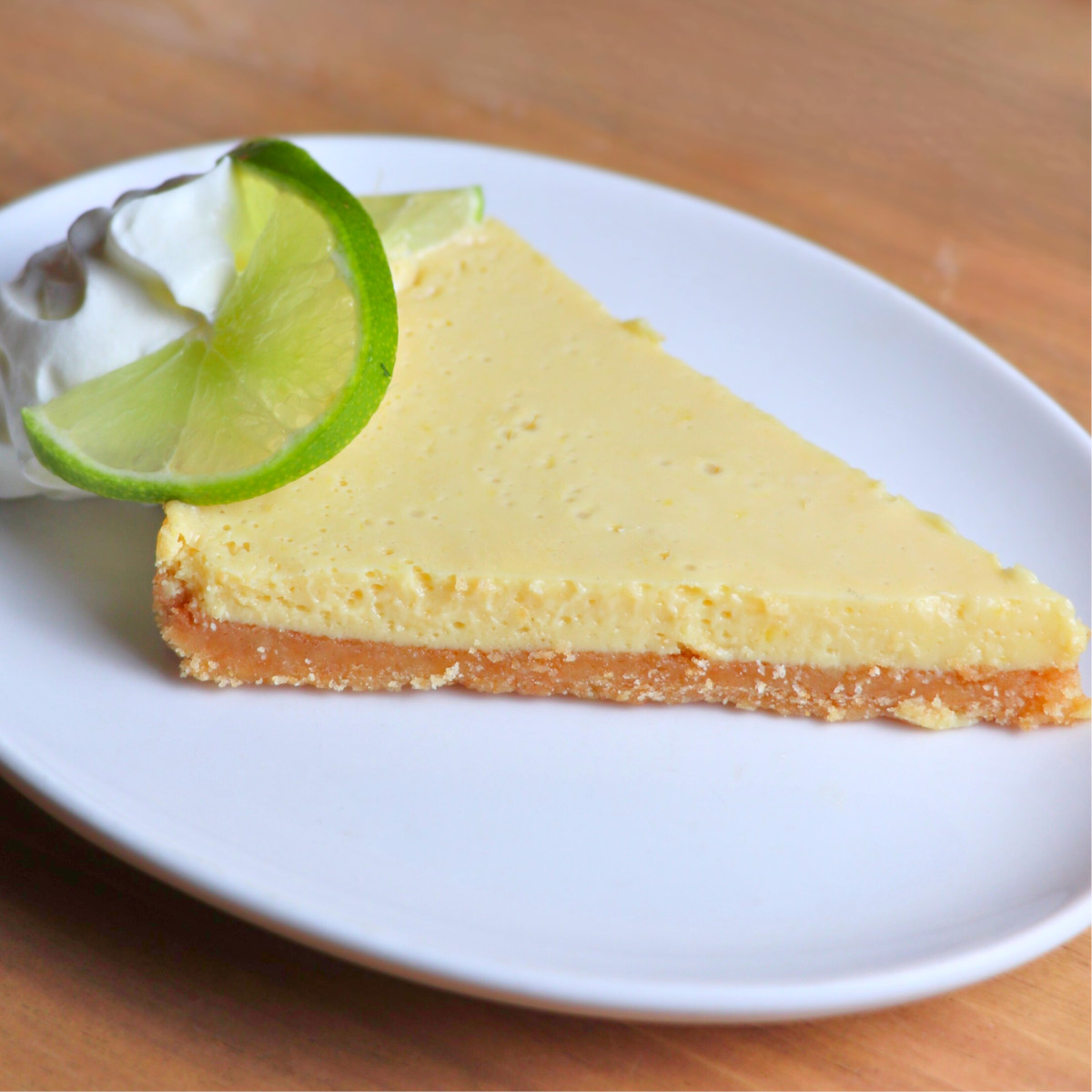 A slice of key lime pie with a lime garnish on a white plate