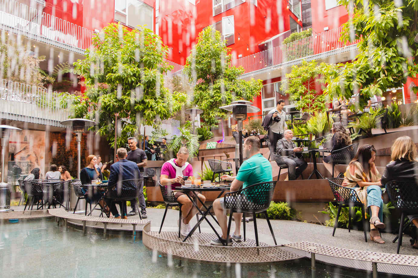 Patrons dining on a lush, open-air restaurant patio with a fountain.