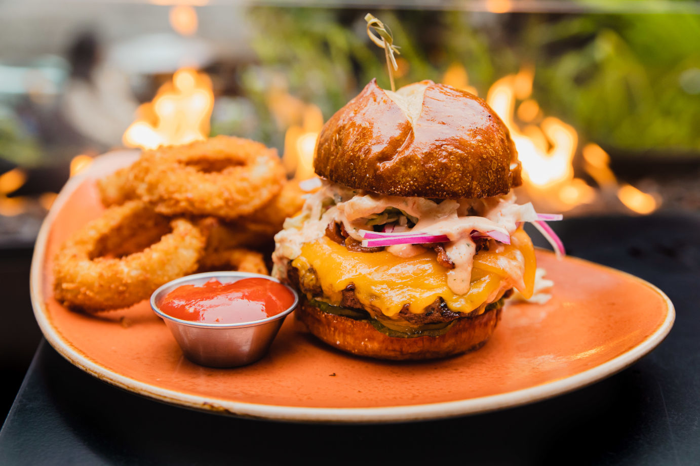 Cheeseburger on a pretzel bun served with a side of crispy onion rings.
