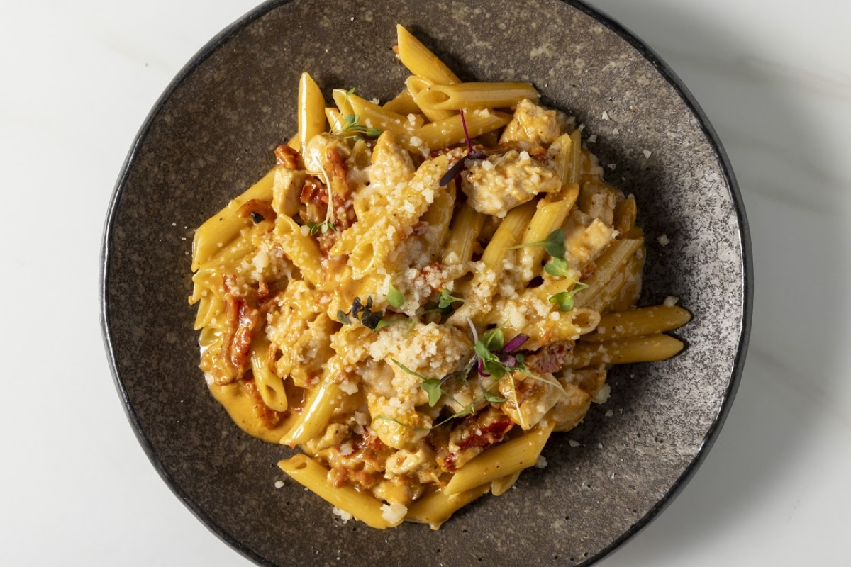 Close-up of creamy penne pasta with chicken, crumbled cheese, and microgreens on a dark plate