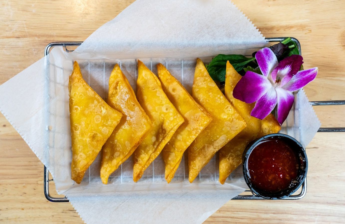 Crispy fried wontons on a rack with sweet chili sauce and an orchid garnish.